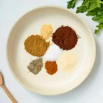 measured spices for chili seasoning in a bowl including chili powder, cumin, paprika, garlic powder, onion powder, salt and pepper