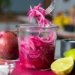 jar of bright pink pickled red onions with a fork lifting onion slices, lime and red onion nearby