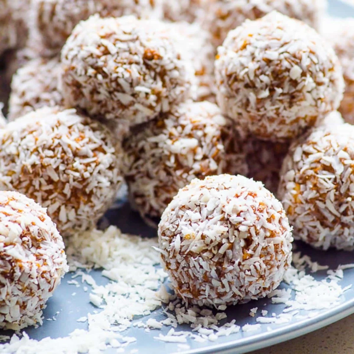 coconut coated protein balls on a plate with shredded coconut scattered around