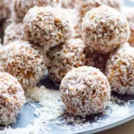 coconut coated protein balls on a plate with shredded coconut scattered around