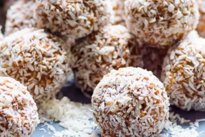 coconut coated protein balls on a plate with shredded coconut scattered around