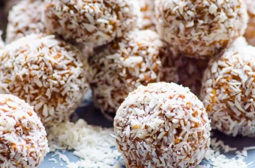 coconut coated protein balls on a plate with shredded coconut scattered around