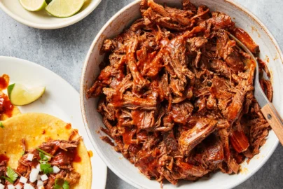 shredded beef barbacoa in a bowl with lime wedges and tacos on the side