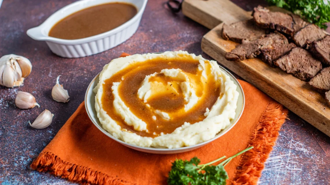 au jus sauce served with mashed potatoes and sliced roast beef on a cutting board