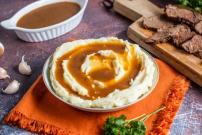 au jus sauce served with mashed potatoes and sliced roast beef on a cutting board
