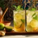 two iced lemon ginger drinks with mint and lime slices on a wooden board with honey and ginger nearby