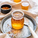 jar of hot honey with red pepper flakes on a tray with a spoon and chili flakes nearby