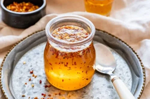 jar of hot honey with red pepper flakes on a tray with a spoon and chili flakes nearby