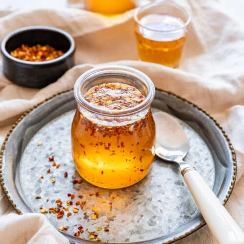 jar of hot honey with red pepper flakes on a tray with a spoon and chili flakes nearby