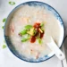creamy rice porridge in a bowl with ginger, green onions, and optional egg topping