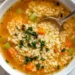 bowl of pastina soup with tiny pasta, carrots, celery and herbs in a clear broth with a spoon