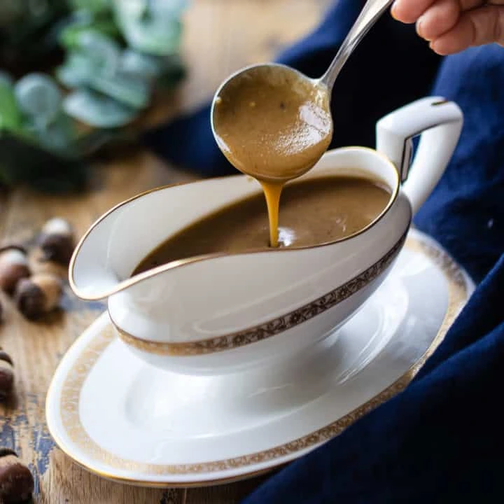 brown gravy being poured from a ladle into a white gravy boat