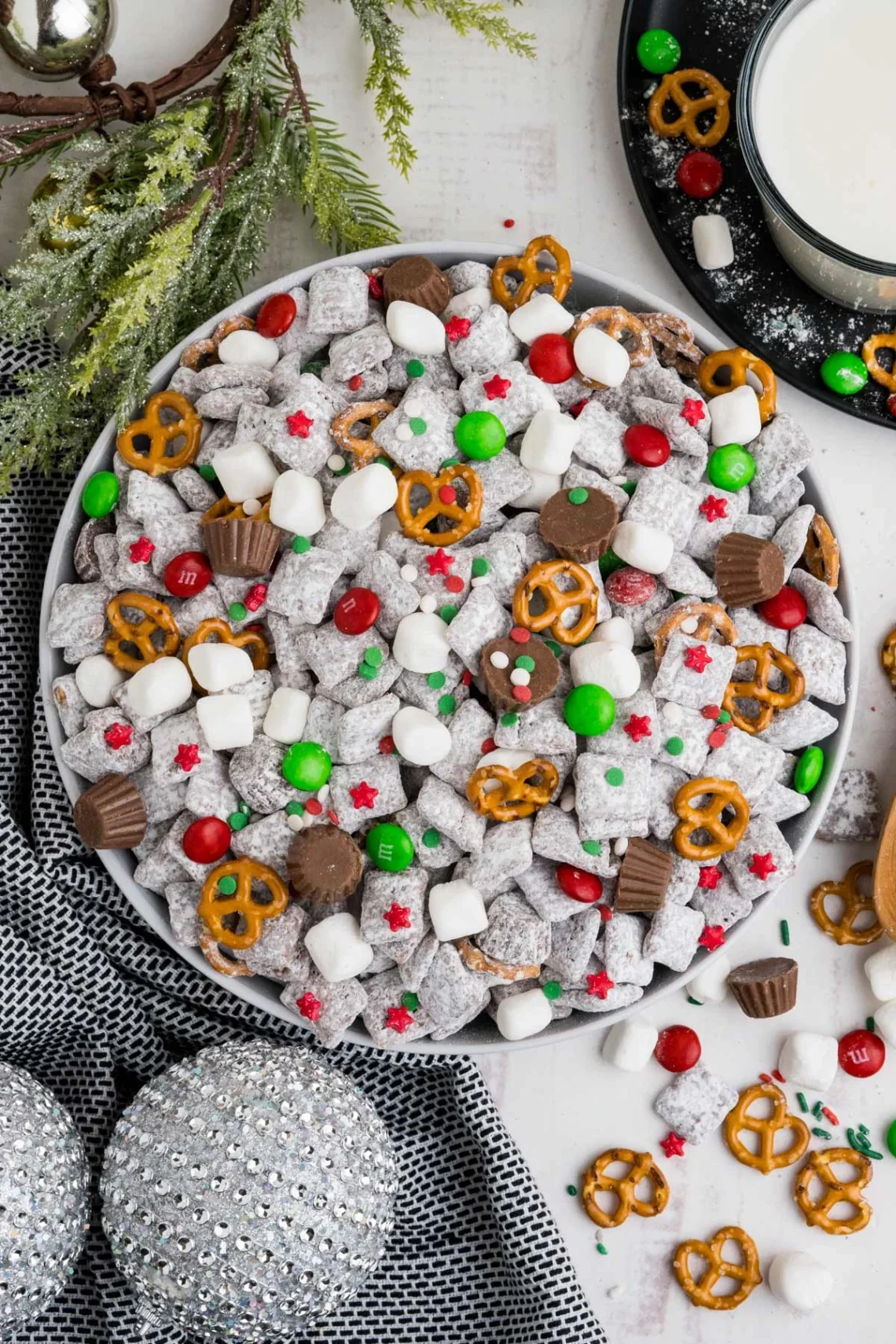 muddy buddy puppy chow mix in a bowl with powdered sugar, pretzels, mini marshmallows and red green candy