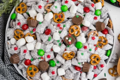 muddy buddy puppy chow mix in a bowl with powdered sugar, pretzels, mini marshmallows and red green candy