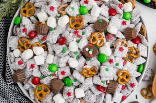 muddy buddy puppy chow mix in a bowl with powdered sugar, pretzels, mini marshmallows and red green candy