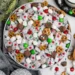 muddy buddy puppy chow mix in a bowl with powdered sugar, pretzels, mini marshmallows and red green candy