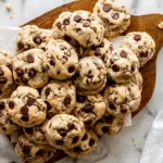 pile of chocolate chip cookies on a wooden board with chocolate chips visible on top