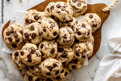 pile of chocolate chip cookies on a wooden board with chocolate chips visible on top