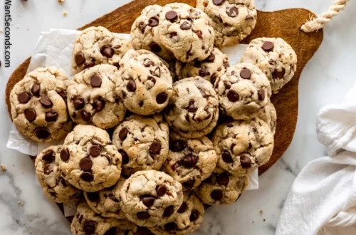 pile of chocolate chip cookies on a wooden board with chocolate chips visible on top