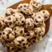 pile of chocolate chip cookies on a wooden board with chocolate chips visible on top