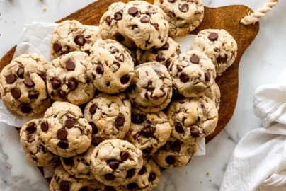 pile of chocolate chip cookies on a wooden board with chocolate chips visible on top