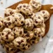 pile of chocolate chip cookies on a wooden board with chocolate chips visible on top