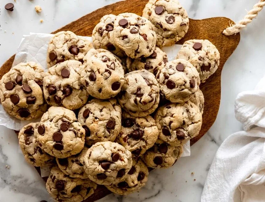 pile of chocolate chip cookies on a wooden board with chocolate chips visible on top