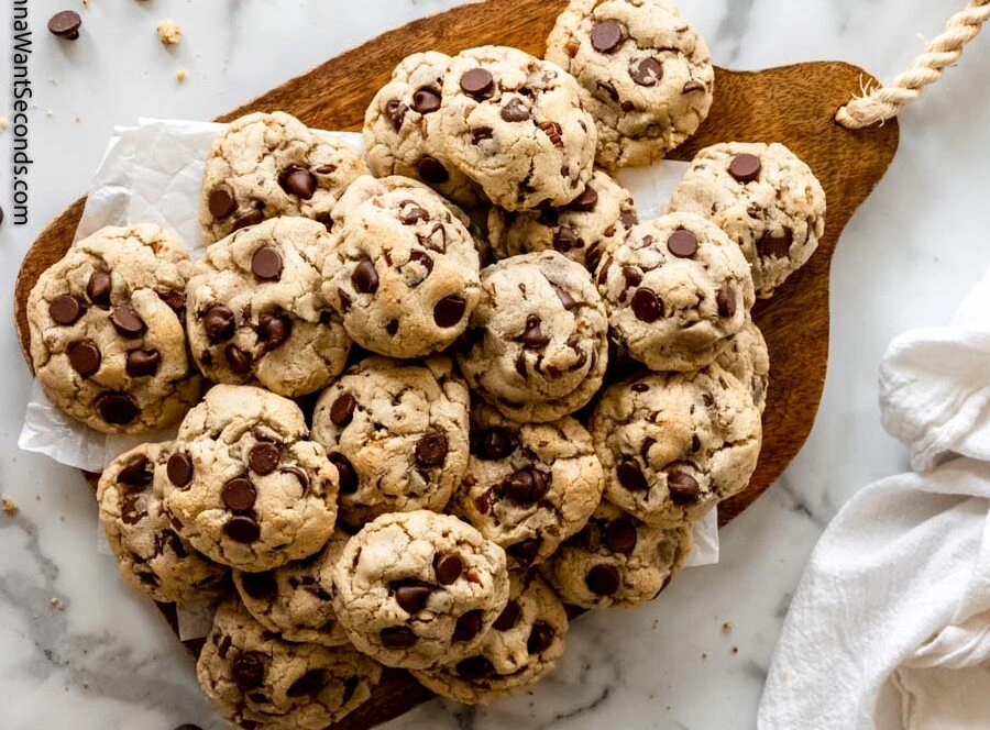 pile of chocolate chip cookies on a wooden board with chocolate chips visible on top