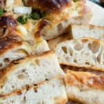 sliced sourdough focaccia bread showing airy holes and golden crust on a wooden board