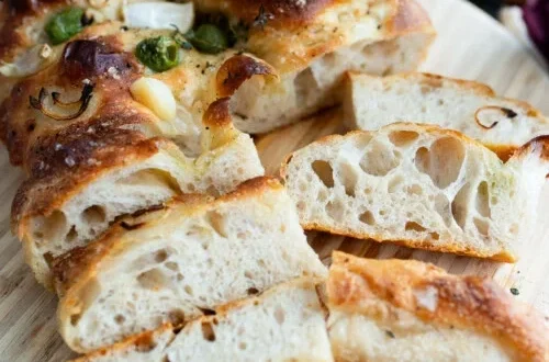 sliced sourdough focaccia bread showing airy holes and golden crust on a wooden board