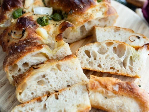 sliced sourdough focaccia bread showing airy holes and golden crust on a wooden board
