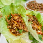 chicken lettuce wraps in crisp lettuce leaves with carrots, herbs, and sesame seeds with filling in a bowl