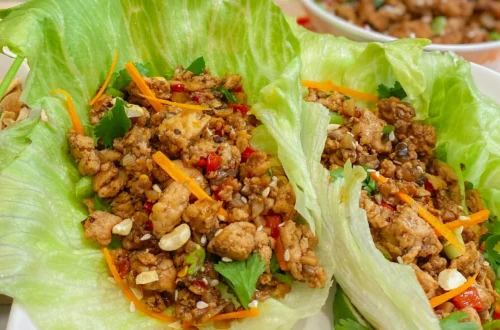 chicken lettuce wraps in crisp lettuce leaves with carrots, herbs, and sesame seeds with filling in a bowl